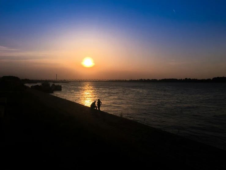 a person standing near the water watching the sun set