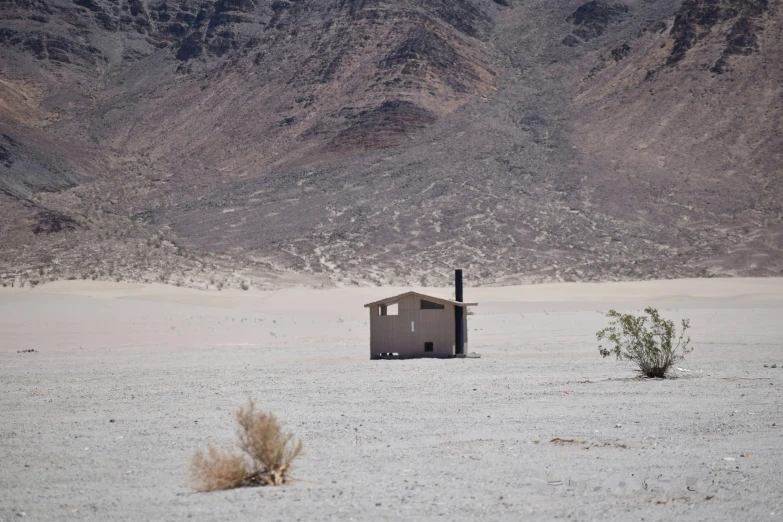 a lone house in a desert with mountains behind it