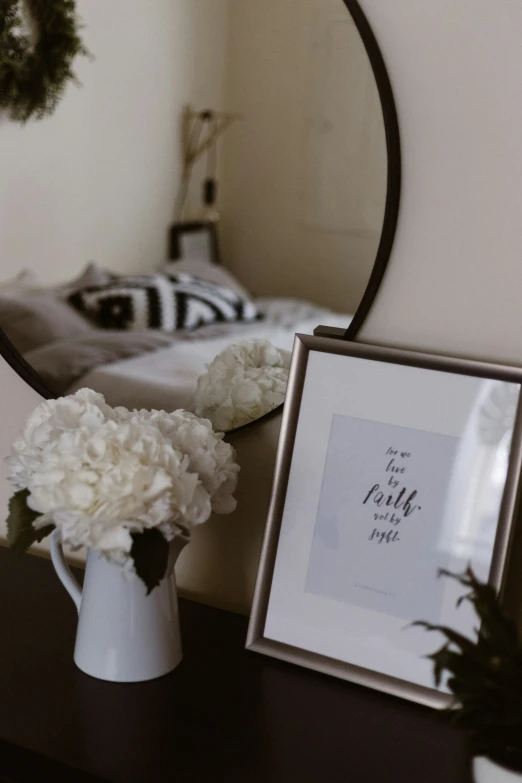 flowers and a picture are sitting on a table next to a bed