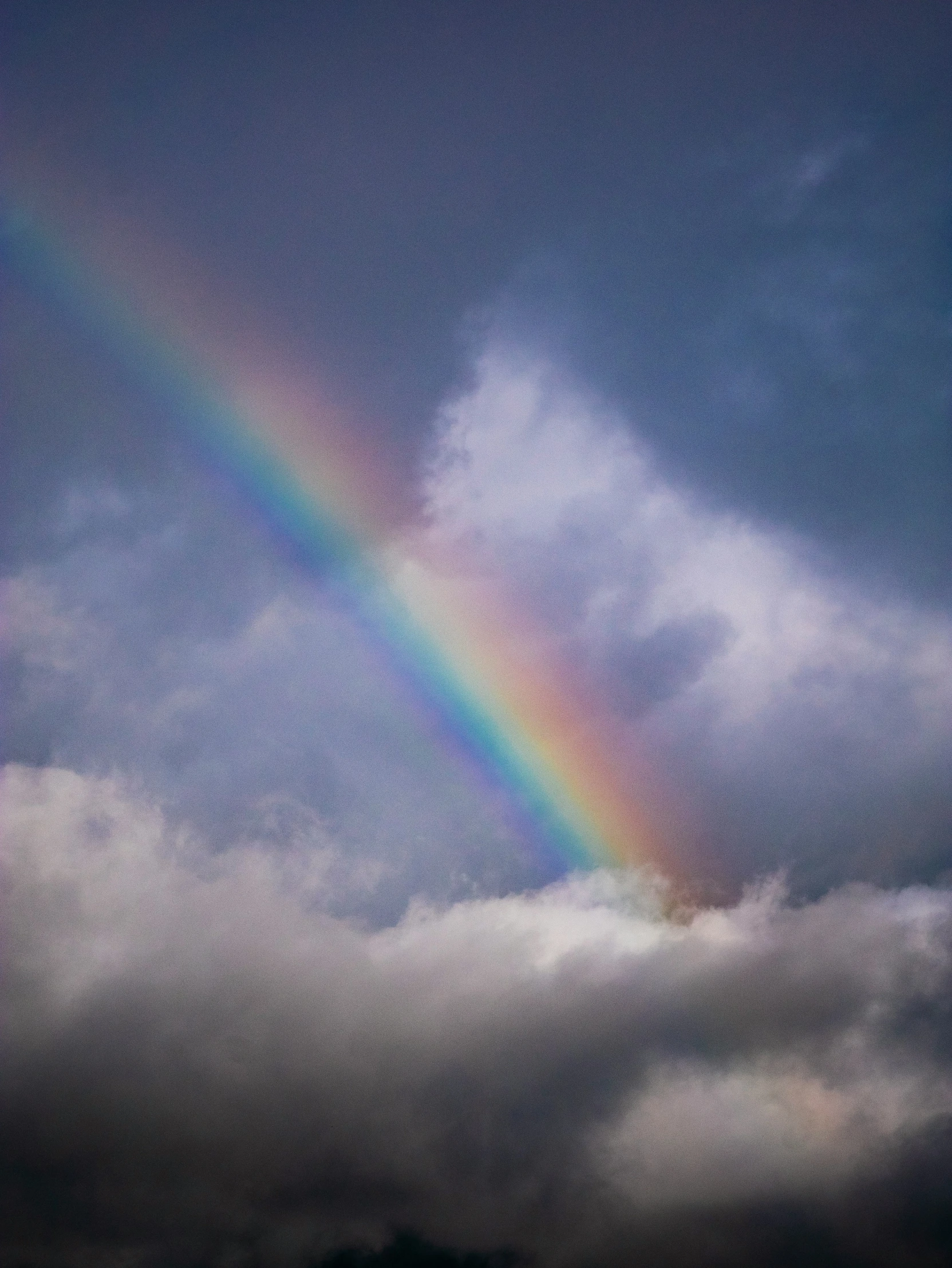a rainbow shines in the middle of a blue cloudy sky
