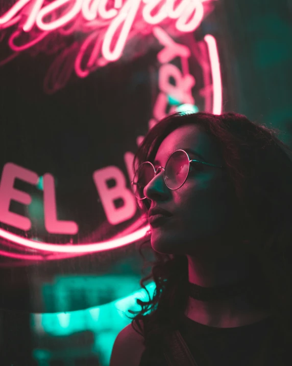 a girl with round glasses standing in front of neon signs