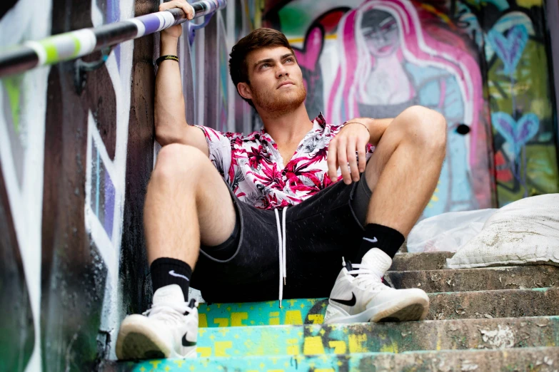 young man sitting down on stairs wearing a colorful shirt