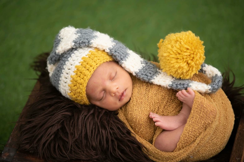 a newborn baby in a knitted hat with a pompom laying on top of grass