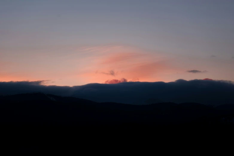 a cloudy sunrise in the sky with a distant mountain top visible