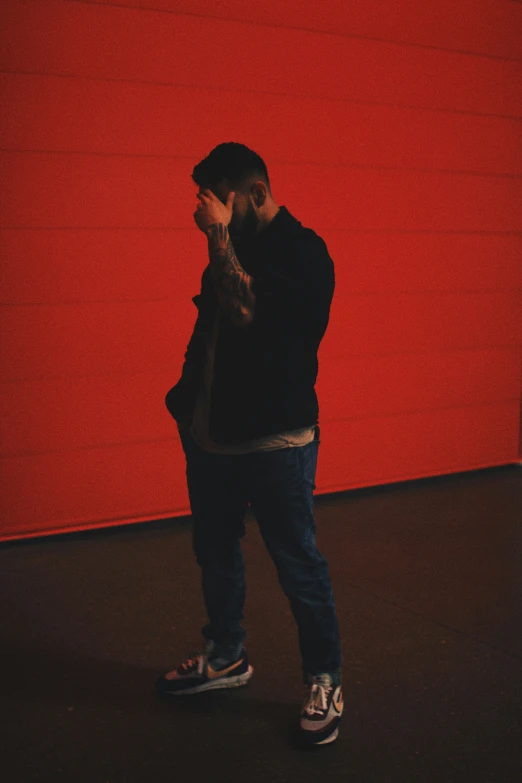 a man stands alone against a red background with his arms behind his head