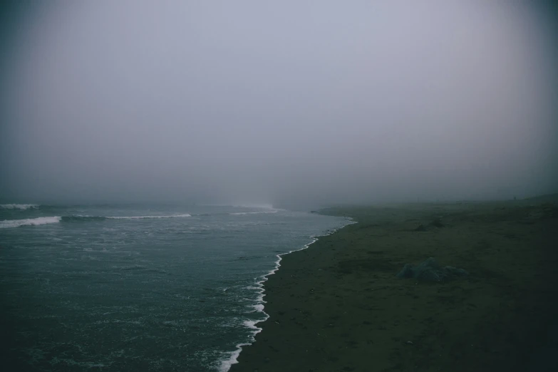 a dark beach is covered in mist and water