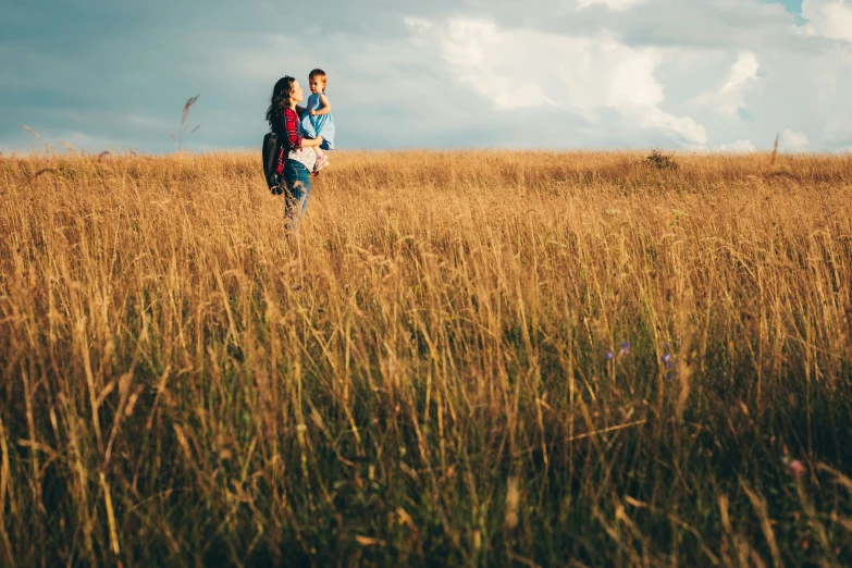 two people walking through tall grass in a large field