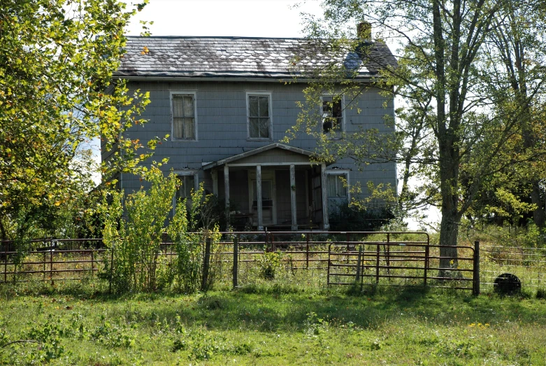 an old gray house sits alone by a field