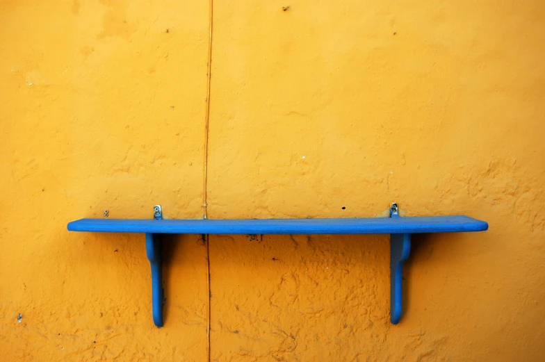 a wooden blue shelf sitting in front of a yellow wall