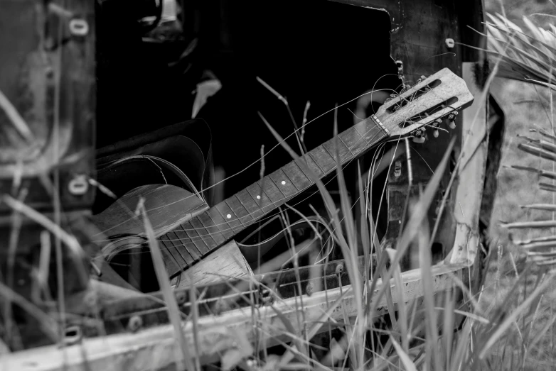 black and white image of a broken acoustic guitar in a hay pile