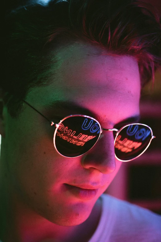 the young man wears bright pink glasses in the dark