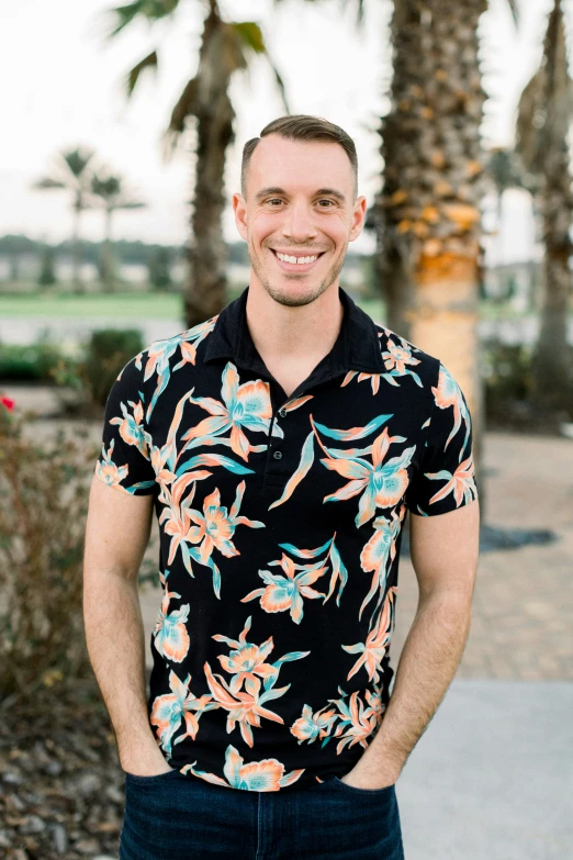 a man with an ugly floral shirt stands smiling