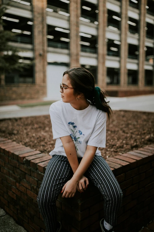 a woman sits against a brick wall, wearing sunglasses