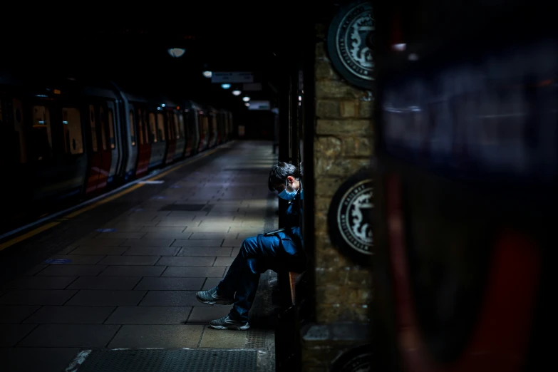 a man in blue jacket sitting on a train platform next to a train