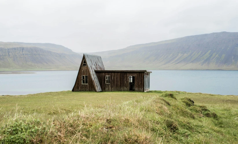 a small cabin in a meadow next to a body of water