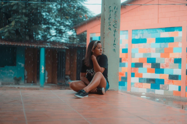 a young person sits on a ground in front of colorful building