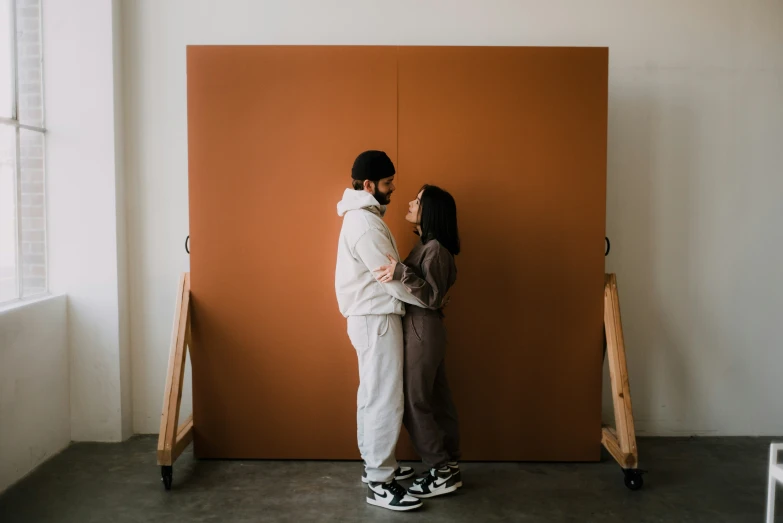 a couple standing next to each other with an orange wall
