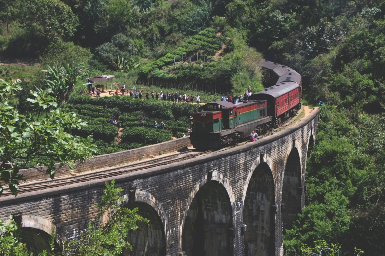 an old train engine with carts goes over a stone bridge