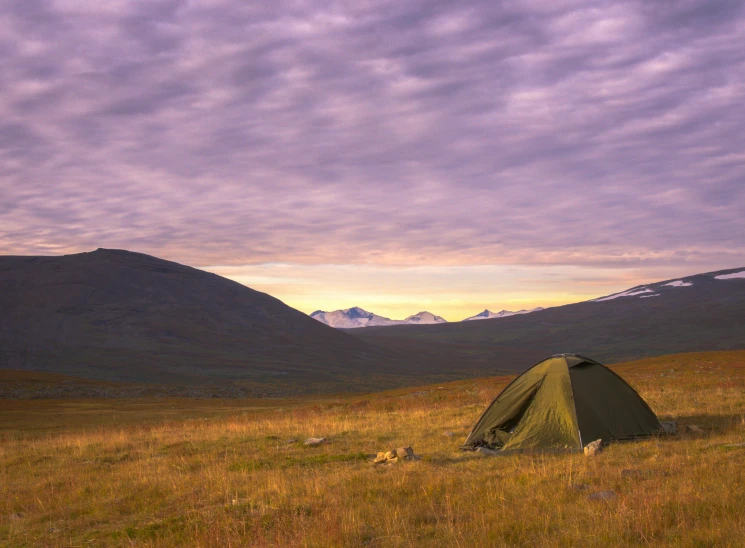 a tent pitched up in the middle of a field with mountains in the background