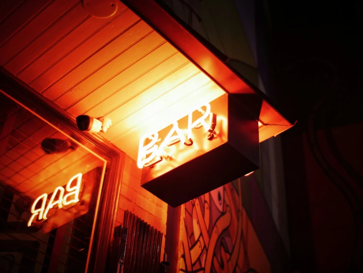 bar neon sign with graffiti above door at night