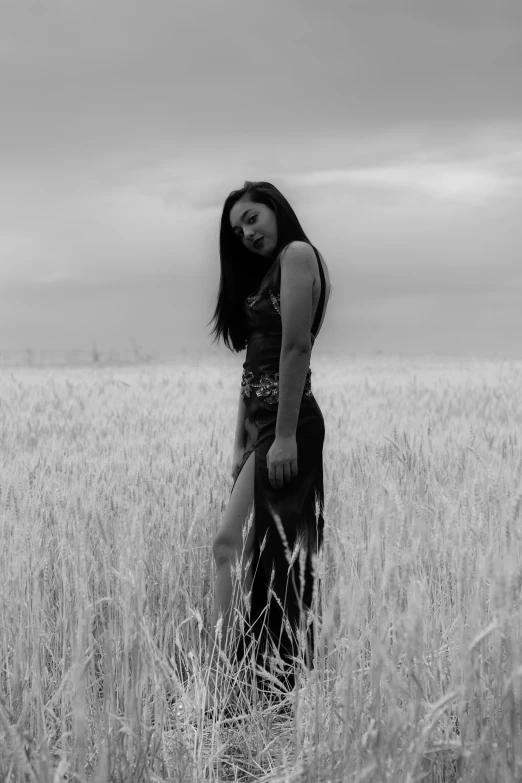 black and white pograph of girl standing in field with cloudy sky