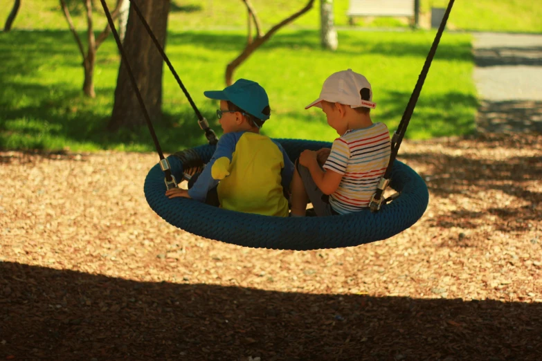 two children sitting on a swing in a park