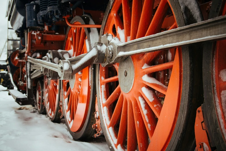 a close up view of the wheels and spokes of an old train in snow