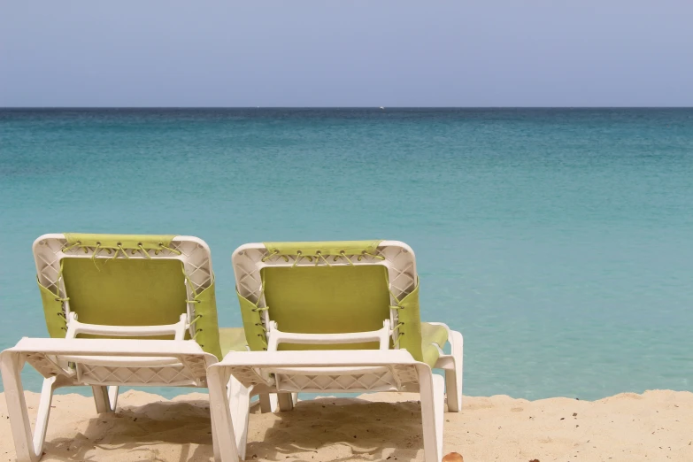 two chairs and two tables that look like the back end of two empty lawn chairs facing the sea