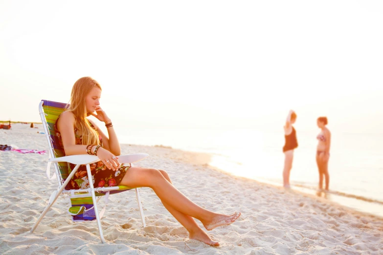 two women and one boy are sitting on a beach, and two are standing on the shore