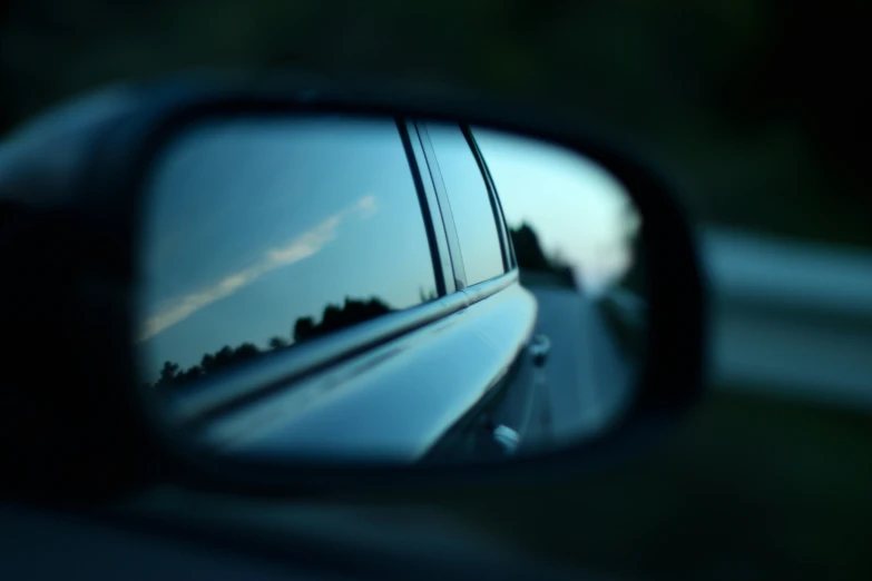 the reflection of trees and mountains in a rear view mirror