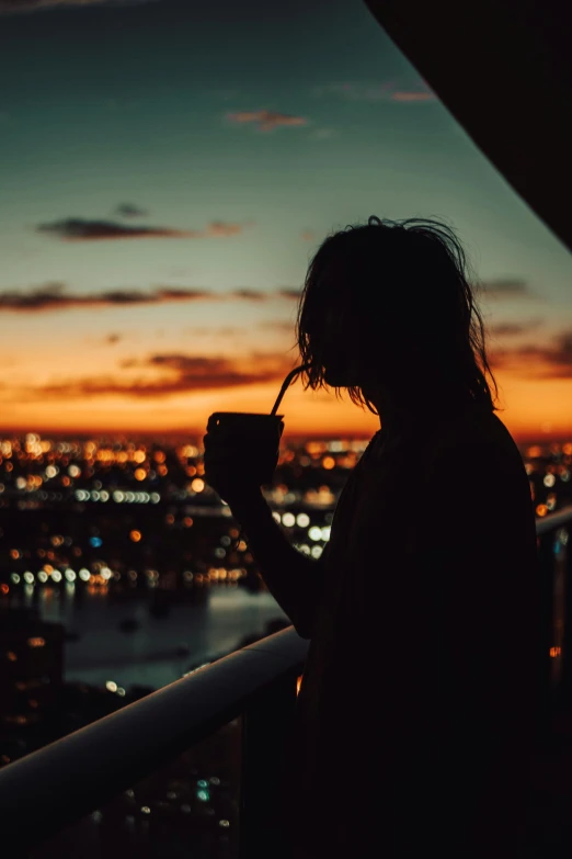 person using cell phone standing on balcony at sunset