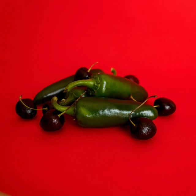 three peppers and four cherries sitting on a red surface