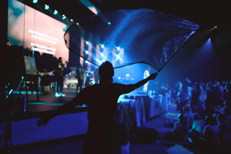 silhouette of person holding umbrella and raising arm on stage