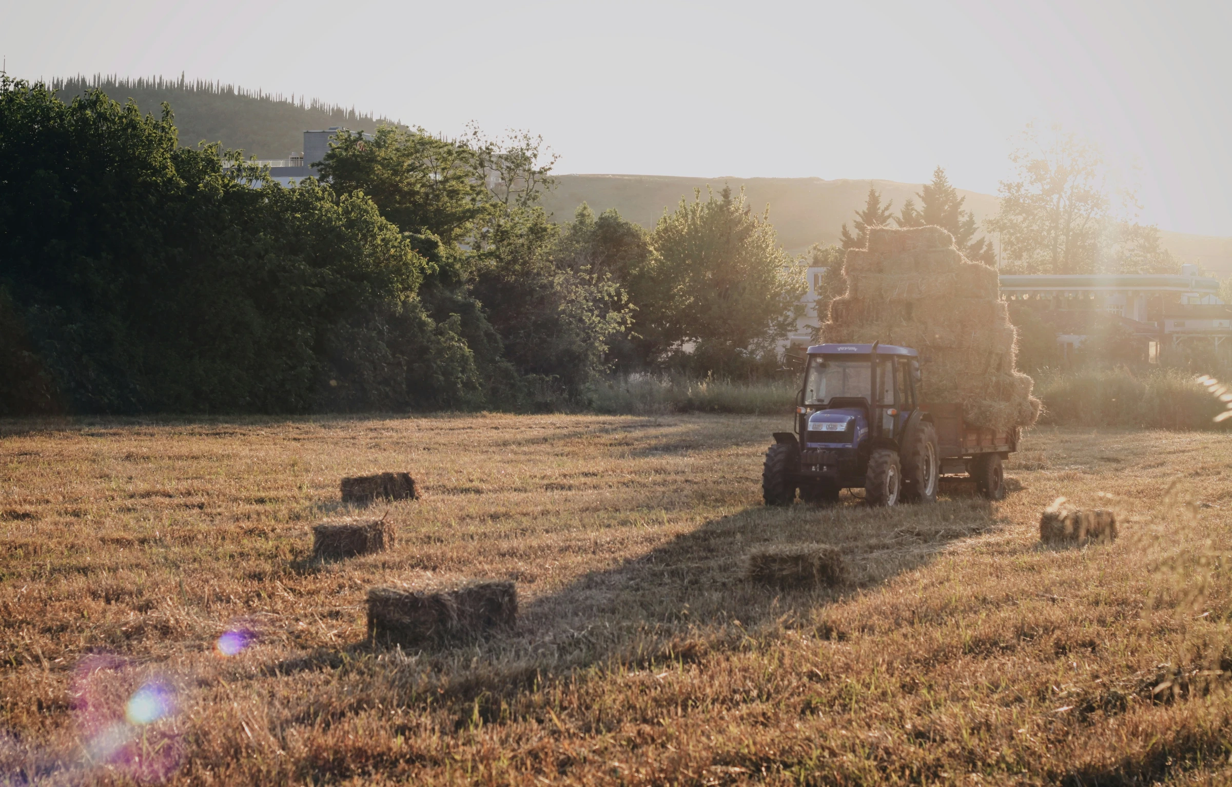 a blue tractor is going across a field with a bale of hay