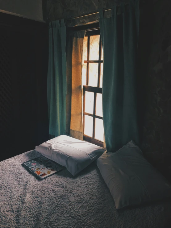 a bed sitting in front of a window next to two pillows