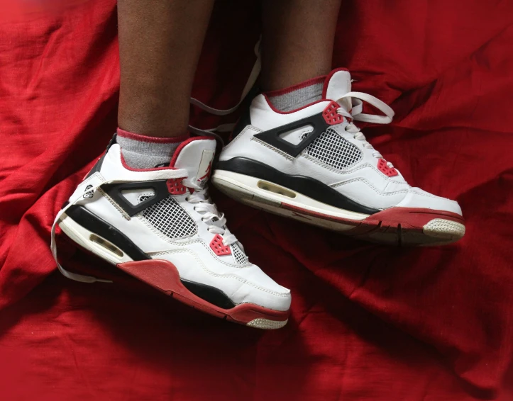 a person sitting on red sheets with sneakers