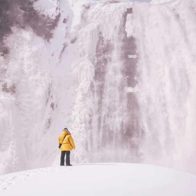 a person standing in the snow near a waterfall