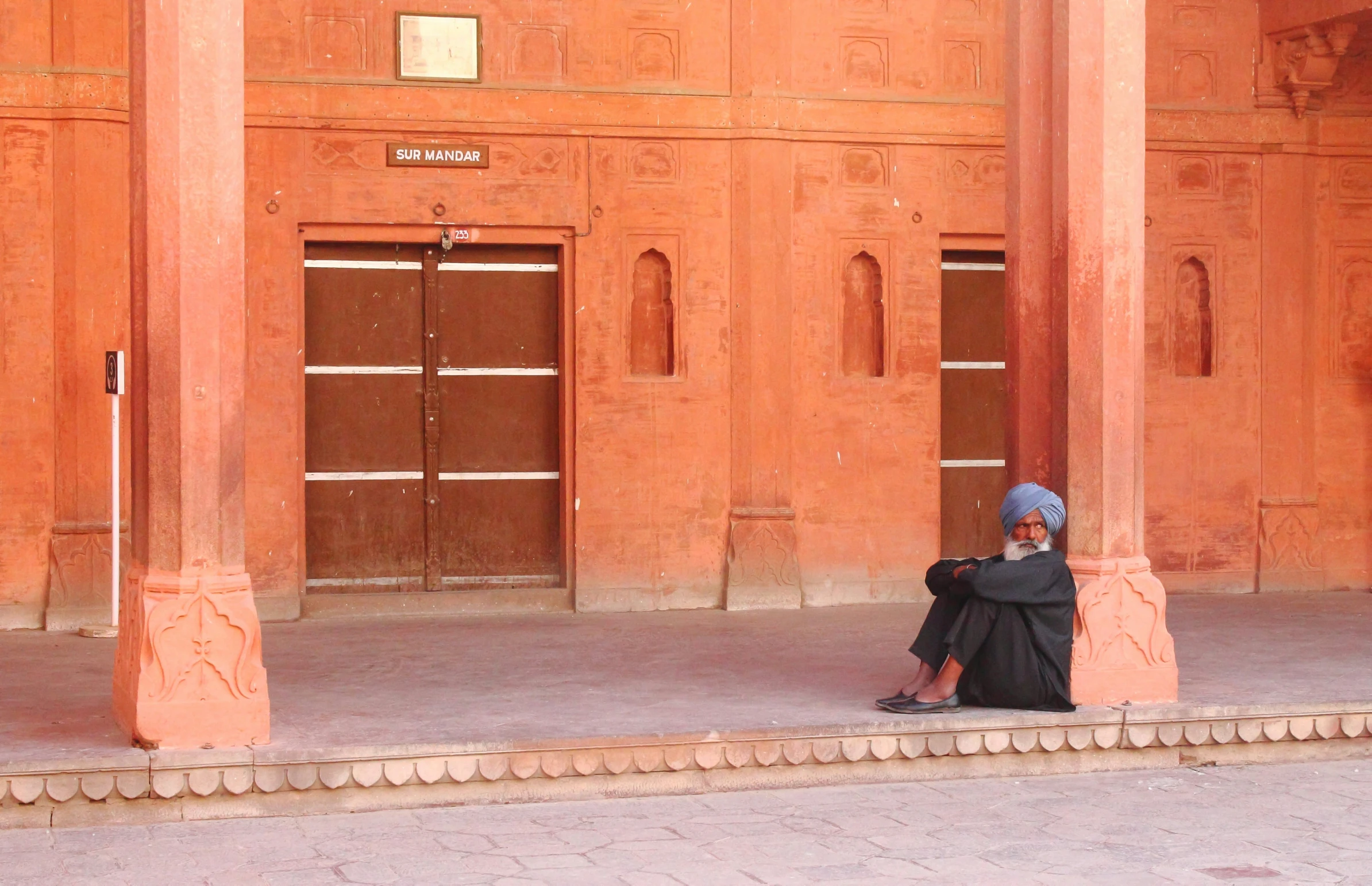 a woman in black sitting on the sidewalk next to an open doorway