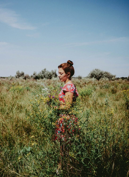 a girl in floral dress walking through a grass covered field