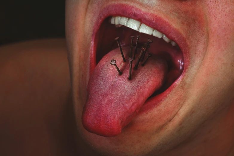 a person has an open tongue and several nails sticking out