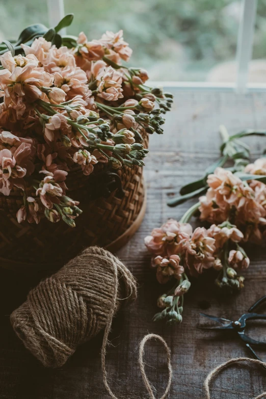 a wooden table with pink flowers next to twine and scissors