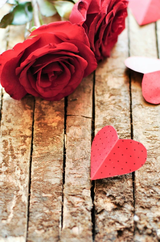 two roses sitting on top of a wooden table next to paper hearts