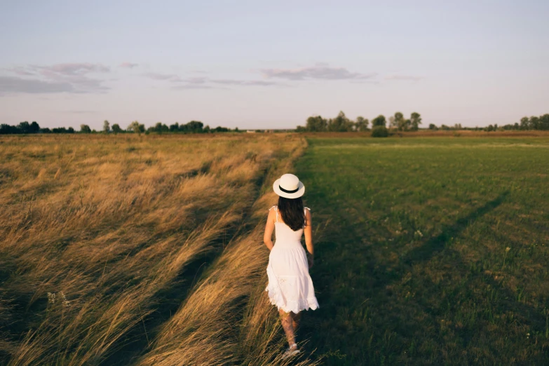 a woman walks along a path through tall grass