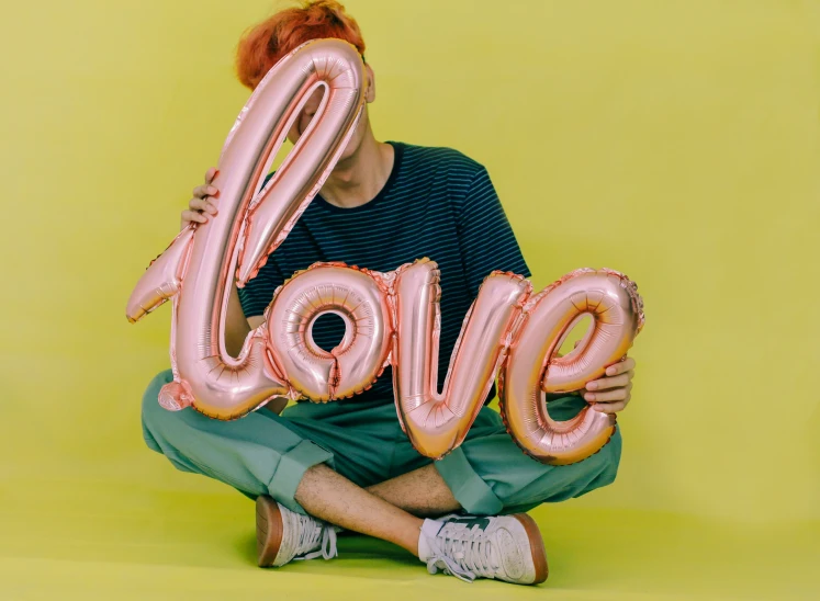 young man posing with large balloons reading love