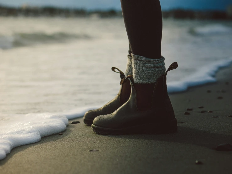 there is a person standing on the beach wearing some boots