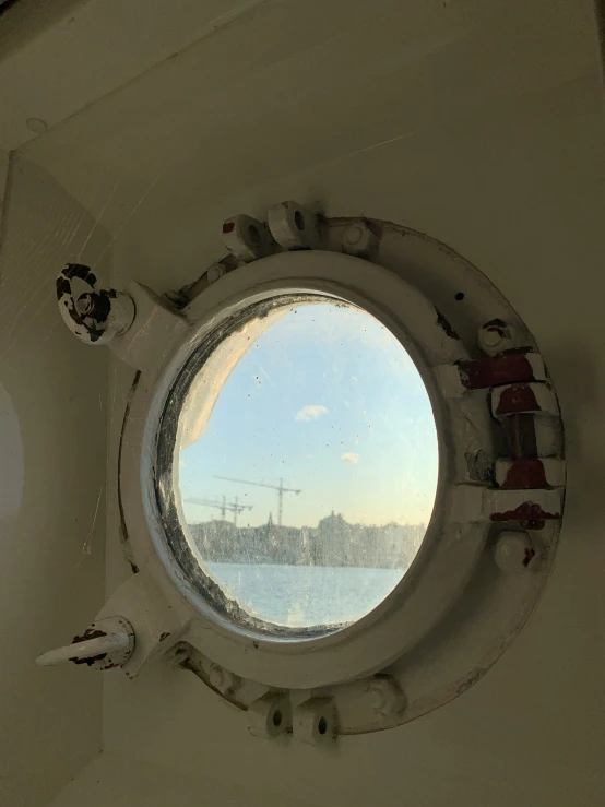 a ship's porthole window with a blue sky and large city in the distance