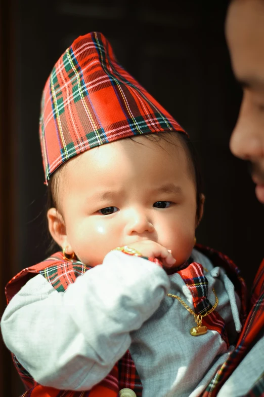 baby wearing red and green tartan hat while being held by mom