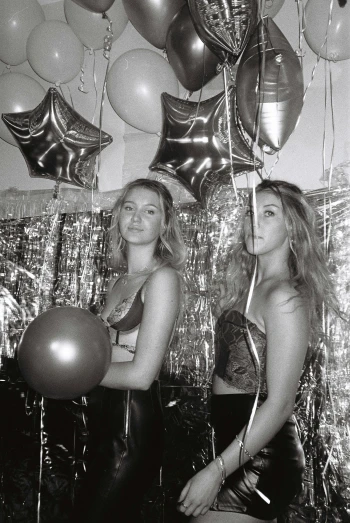 three young women pose for the camera with balloons and streamers hanging from the ceiling