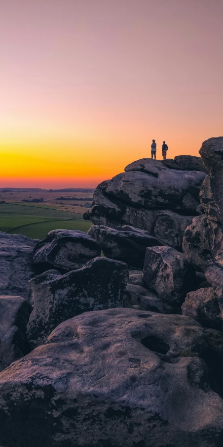 two people on a rock cliff overlooking a sunset