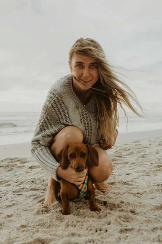 young woman in sweater holding dog on the beach